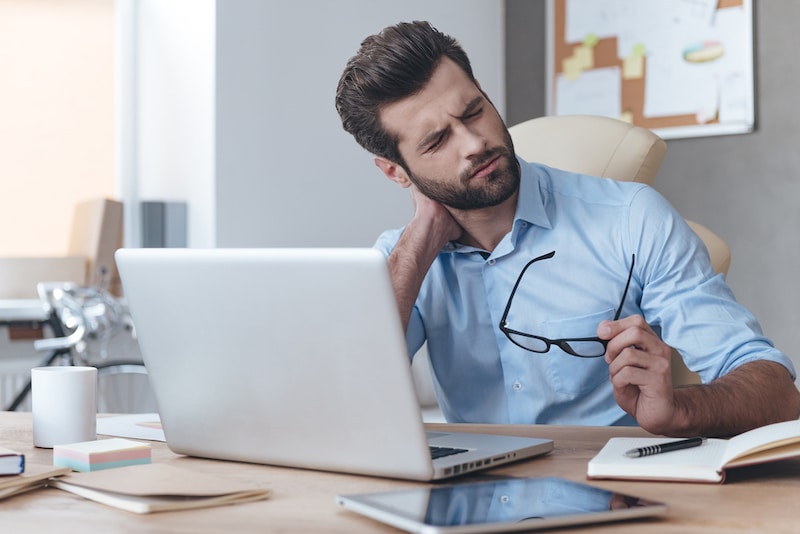 Man Sitting At The Table Holding His Next In Pain