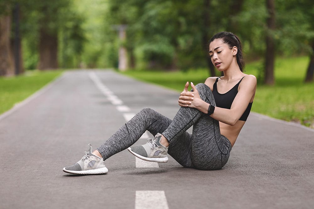 Woman Sitting On The Ground Holding Her Knee In Pain